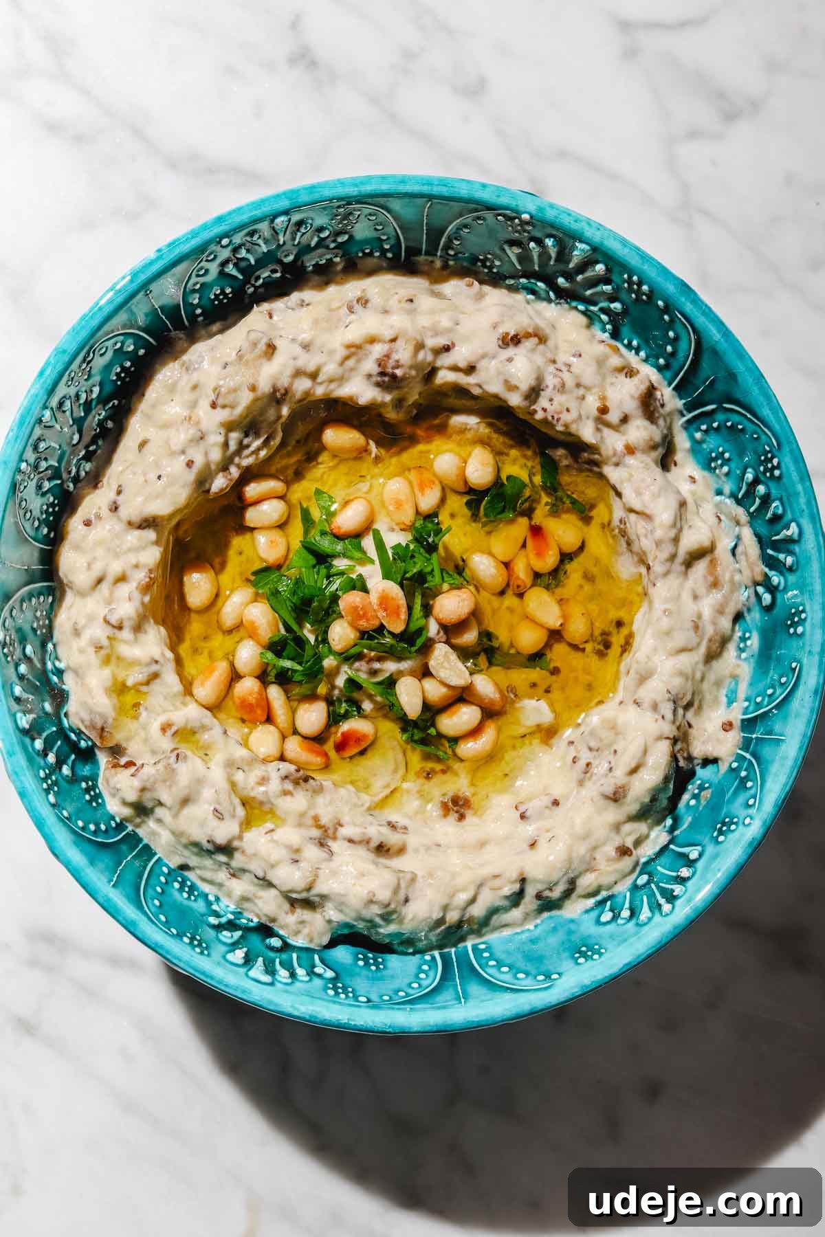 Smoky Mutabal: A Creamy Tahini Treat 13 Mutabal in a blue patterned bowl with olive oil, pine nuts and parsley on a light marble background