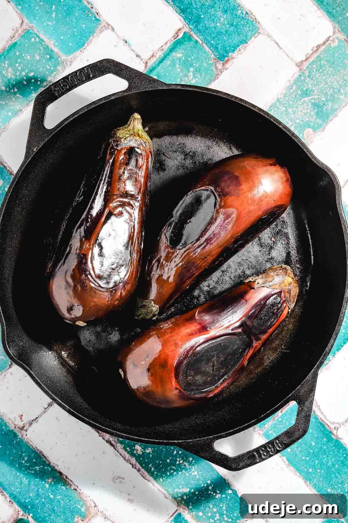 Smoky Mutabal: A Creamy Tahini Treat 3 Three eggplants that have been charred in a cast iron pan on a teal and white brick background