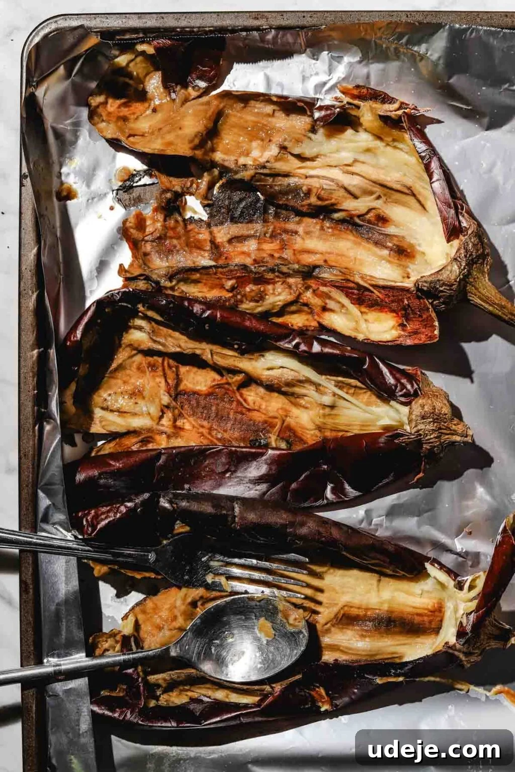 Smoky Mutabal: A Creamy Tahini Treat 8 3 large roasted eggplants that have been split open with the flesh scooped out on a foil lined baking sheet with a spoon and a fork in the bottom eggplant