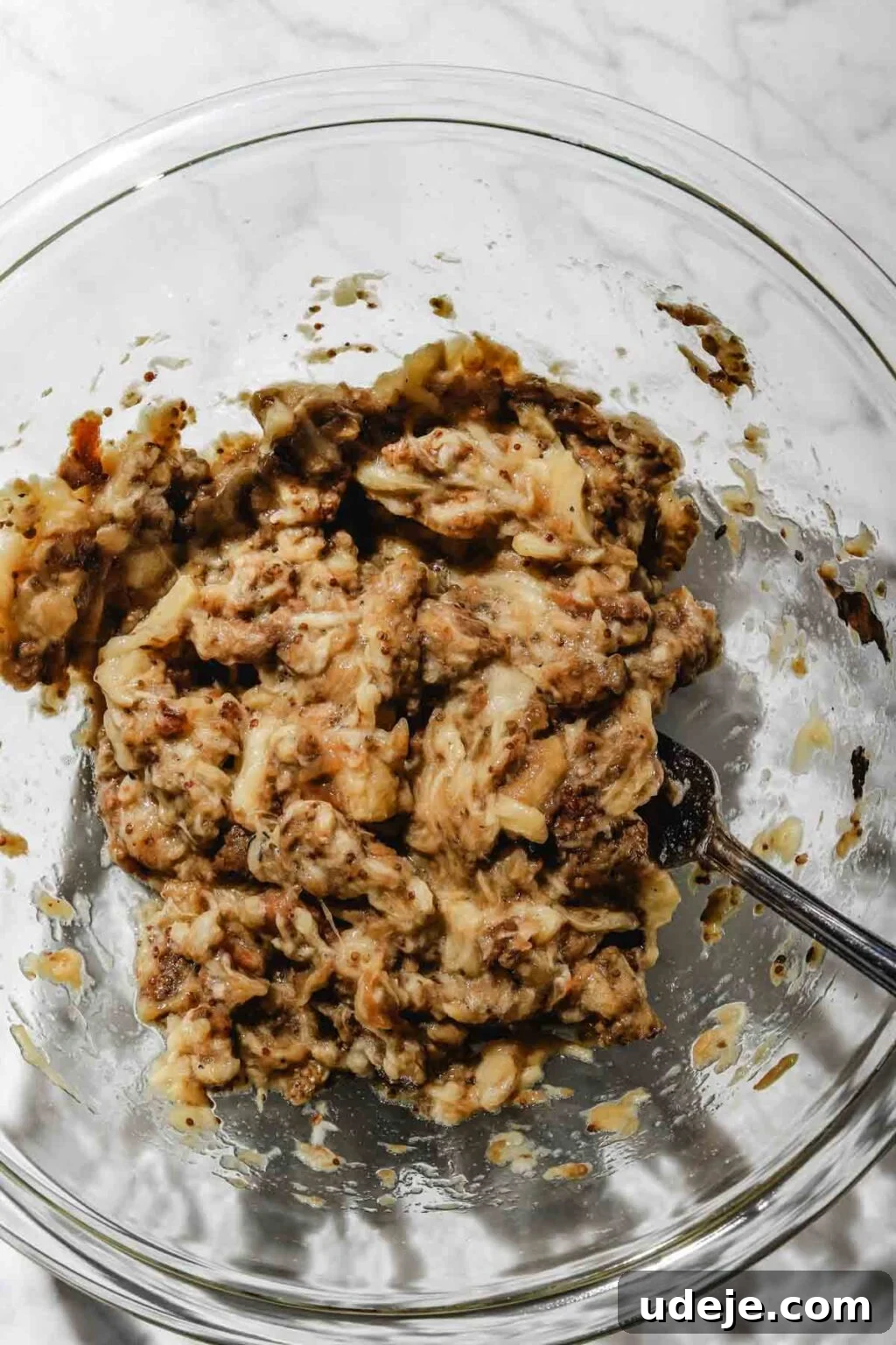Smoky Mutabal: A Creamy Tahini Treat 10 Roasted eggplant flesh mashed in a large glass bowl with a fork in it on a light marble background