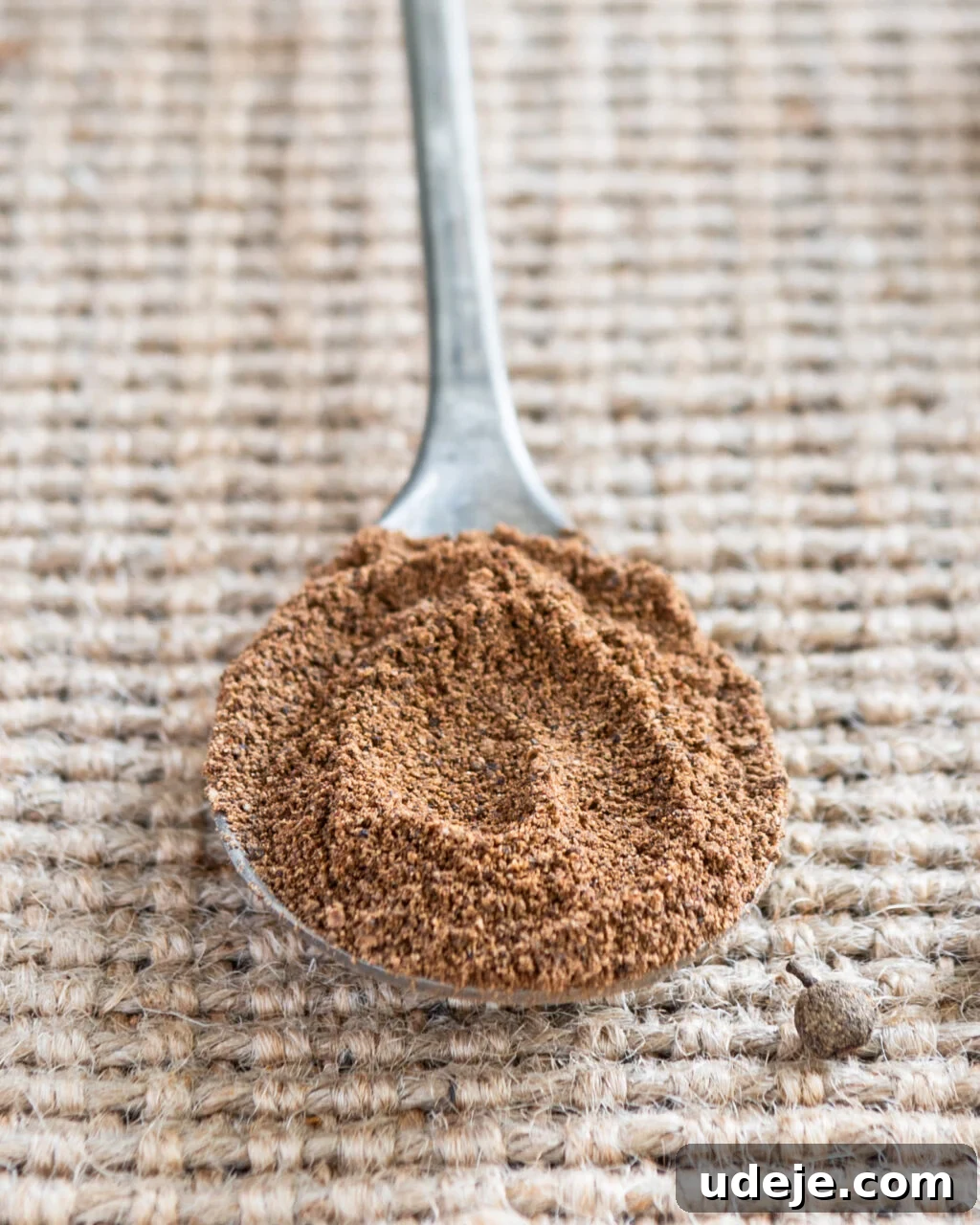 Unlocking the Flavors of Allspice in Middle Eastern Dishes 8 Ground allspice on a metal spoon on a beige woven background