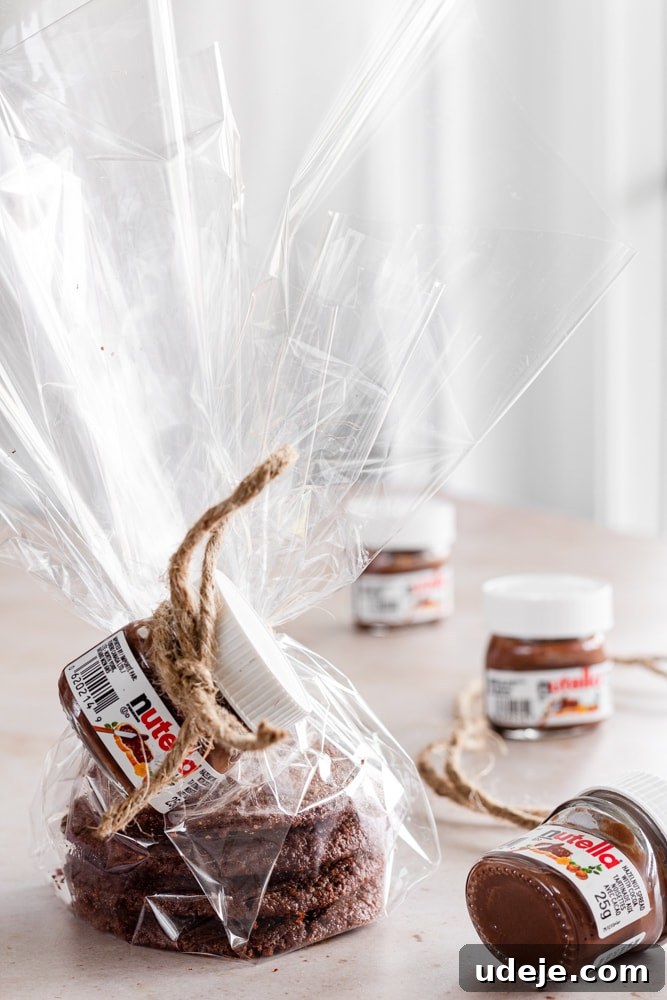 Nutella Cookie Bliss in 15 Minutes 7 Nutella cookies stacked and wrapped in clear plastic, with a mini Nutella jar tied to it. Three mini Nutella jars to the right of the photo