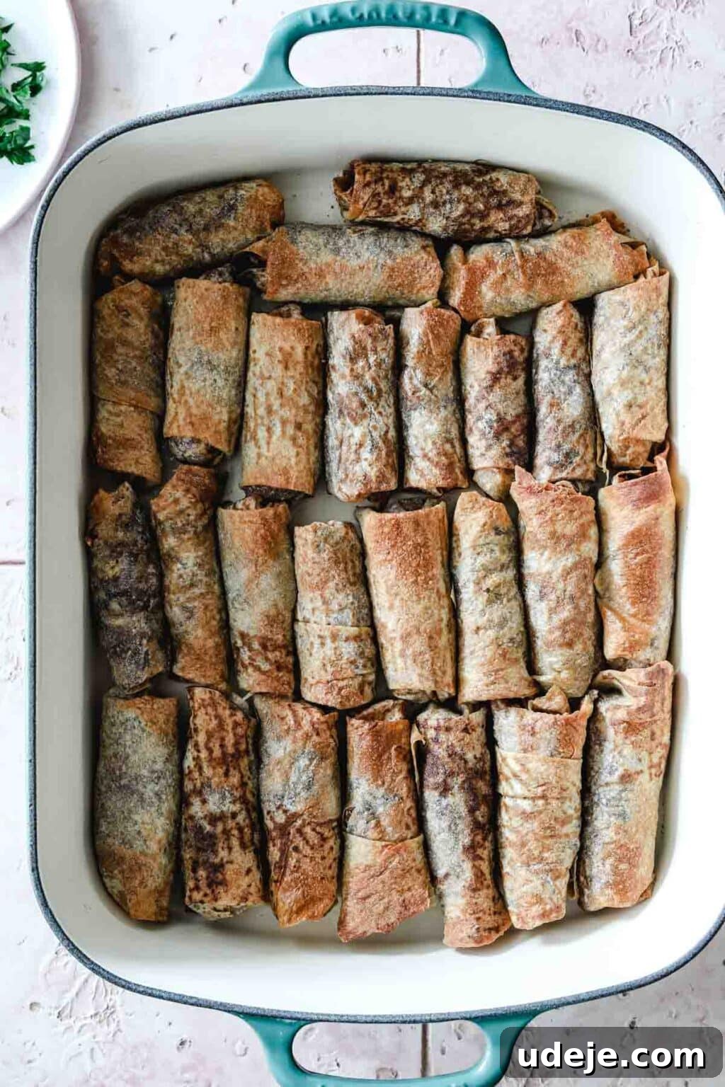 Sumac-Spiced Chicken Musakhan Crisps 3 Baked Musakhan rolls in a teal and white coloured baking dish on a light coloured tiled background, ready to be served