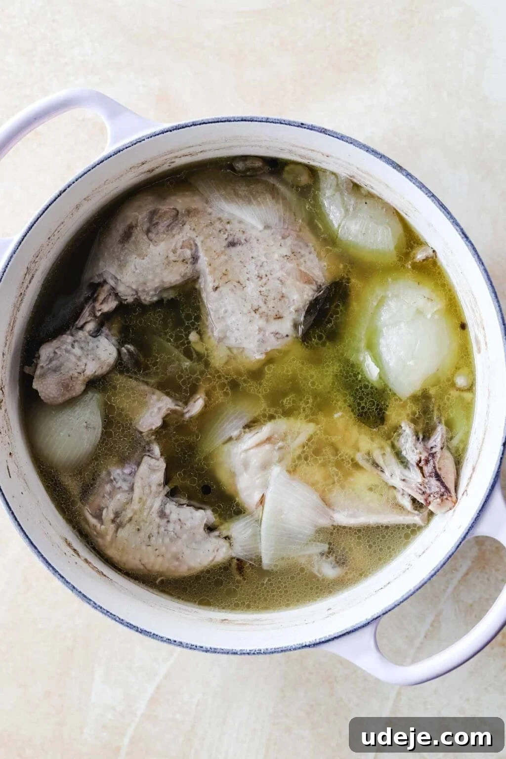 Sumac-Spiced Chicken Musakhan Crisps 8 Chicken legs and thighs simmering in broth with onions and bay leaves in a white pot on a light coloured background, forming a rich base.