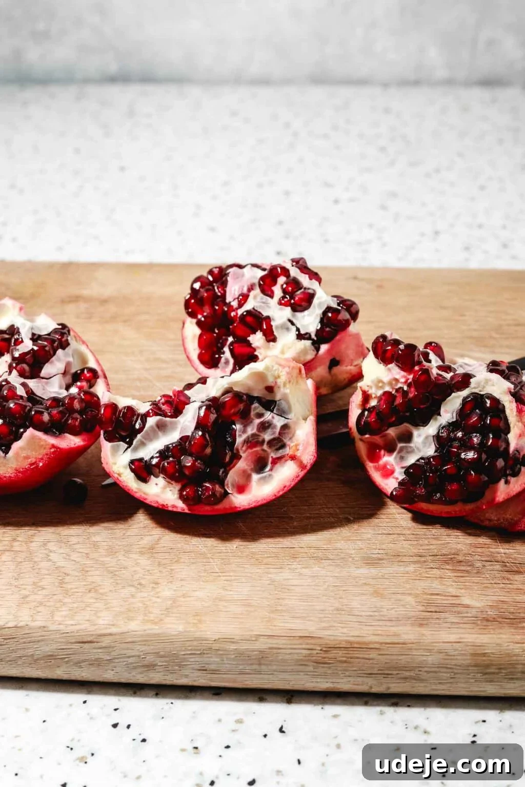 Homemade Pomegranate Molasses: Sweet, Tangy, and Versatile 11 pieces of a whole pomegranate cut up on a wooden cutting board on a speckled background