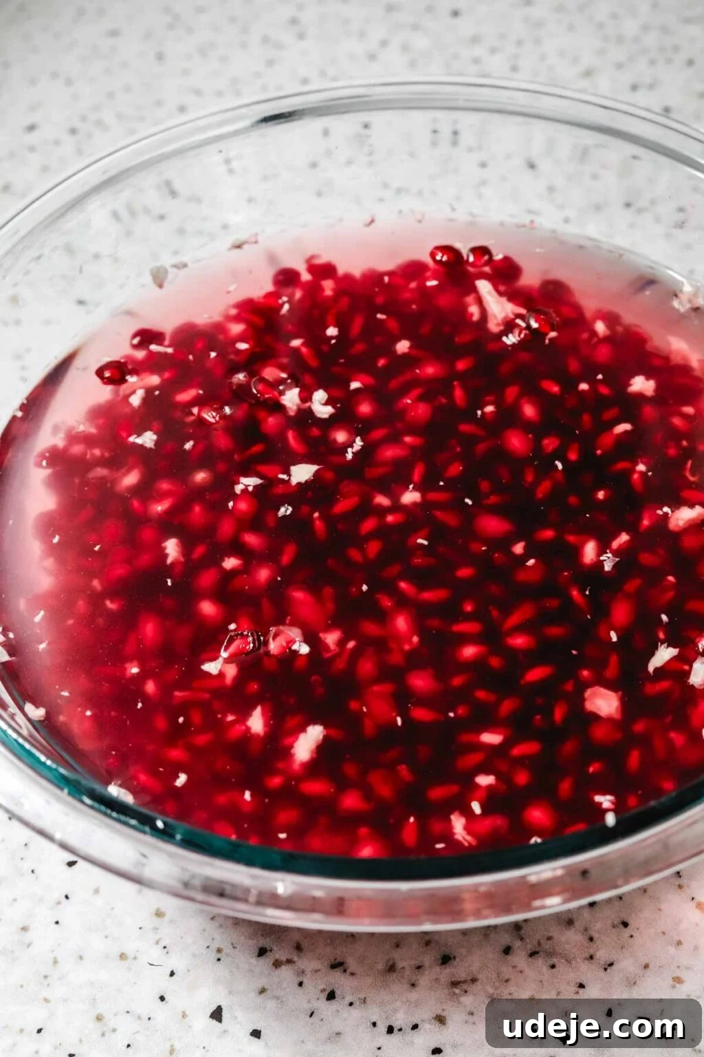 Homemade Pomegranate Molasses: Sweet, Tangy, and Versatile 15 pomegranate seeds in a glass bowl filled with water on a speckled background