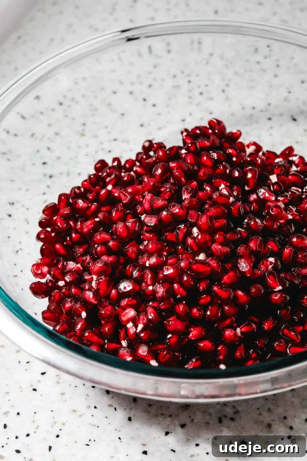 Homemade Pomegranate Molasses: Sweet, Tangy, and Versatile 16 pomegranate seeds in a glass bowl on a speckled background