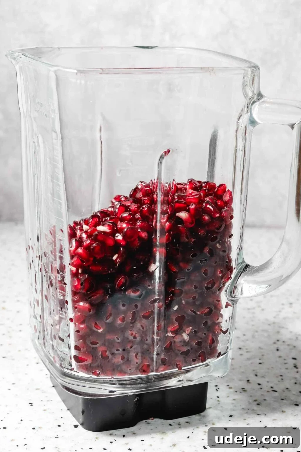 Homemade Pomegranate Molasses: Sweet, Tangy, and Versatile 17 glass blender filled with pomegranate seeds on a speckled background