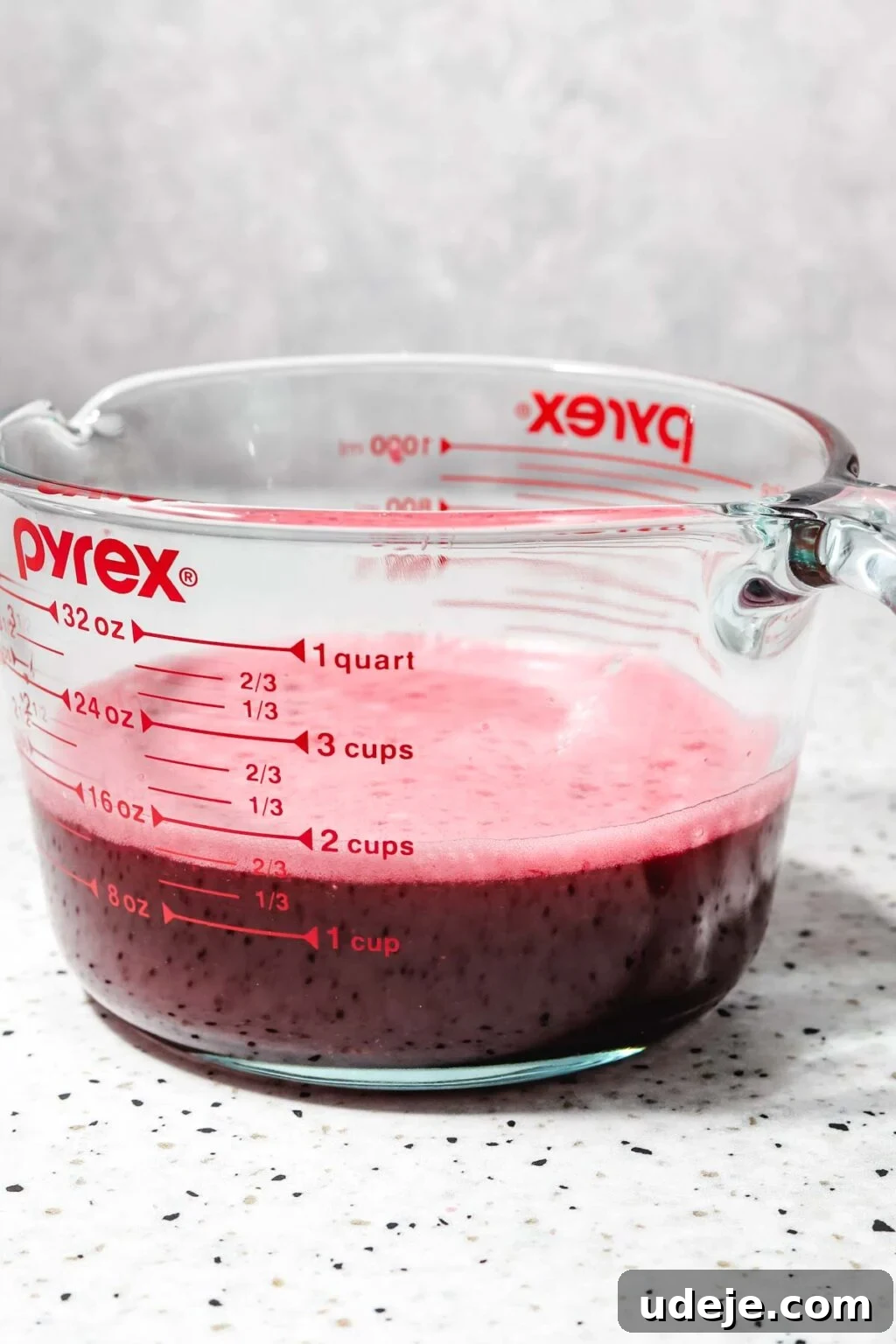 Homemade Pomegranate Molasses: Sweet, Tangy, and Versatile 20 strained blended pomegranate juice in a large measuring cup on a speckled background