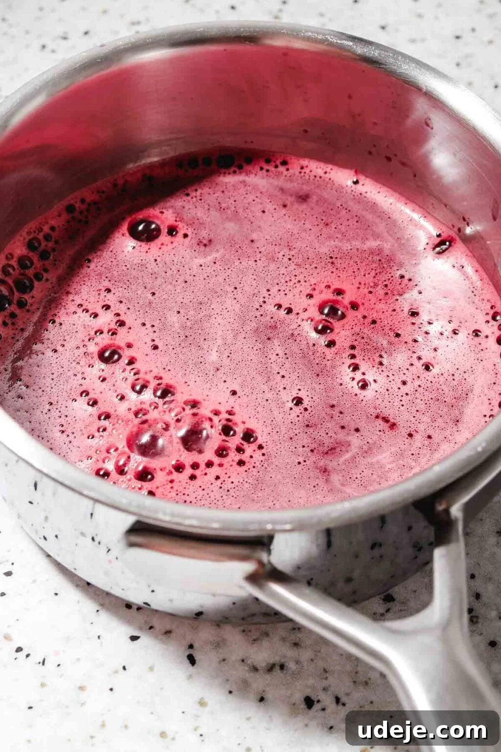 Homemade Pomegranate Molasses: Sweet, Tangy, and Versatile 21 strained blended pomegranate juice in a metal saucepan on a speckled background