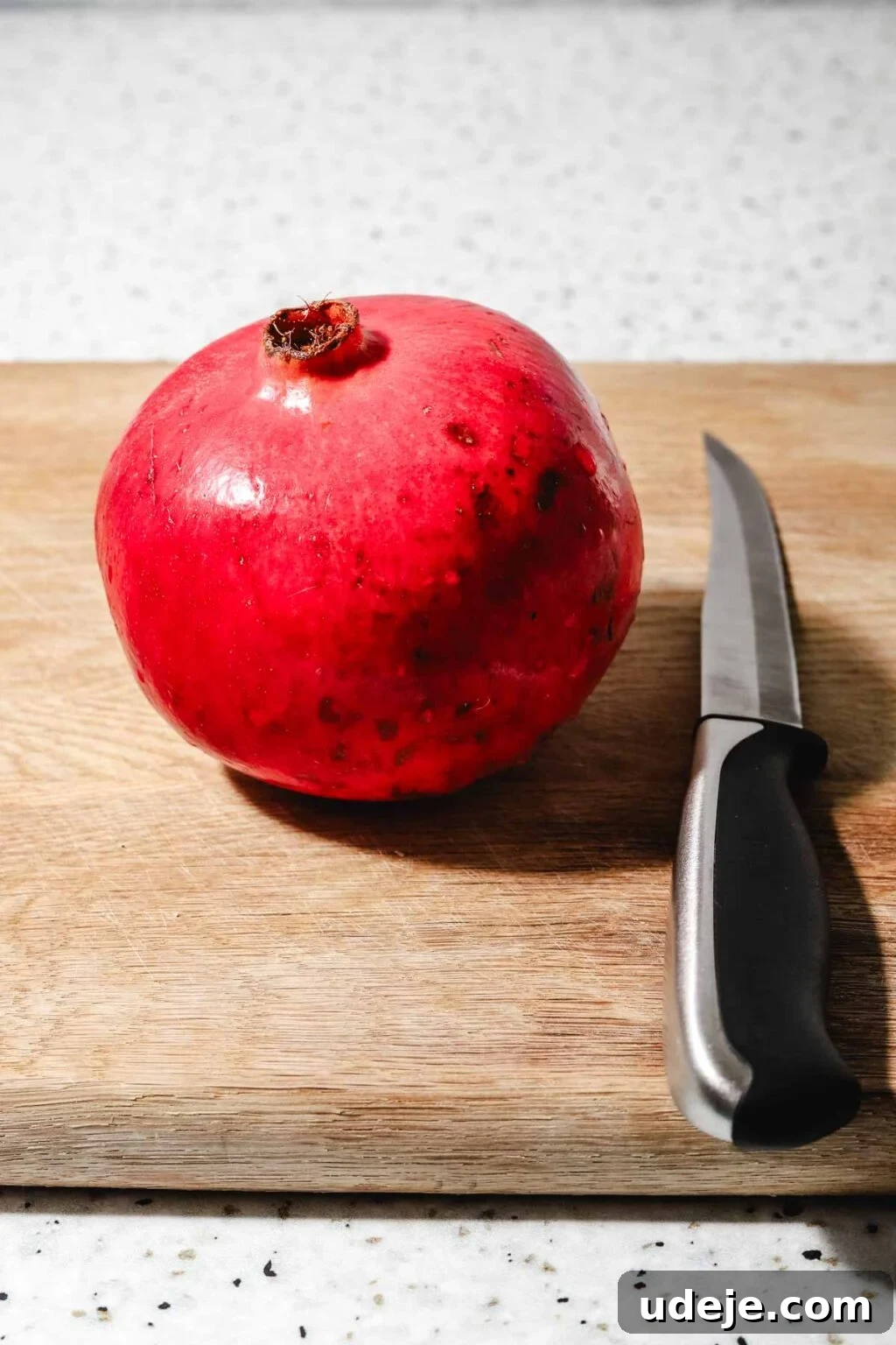 Homemade Pomegranate Molasses: Sweet, Tangy, and Versatile 7 Whole pomegranate on a light wooden cutting board with a knife beside it on a speckled background