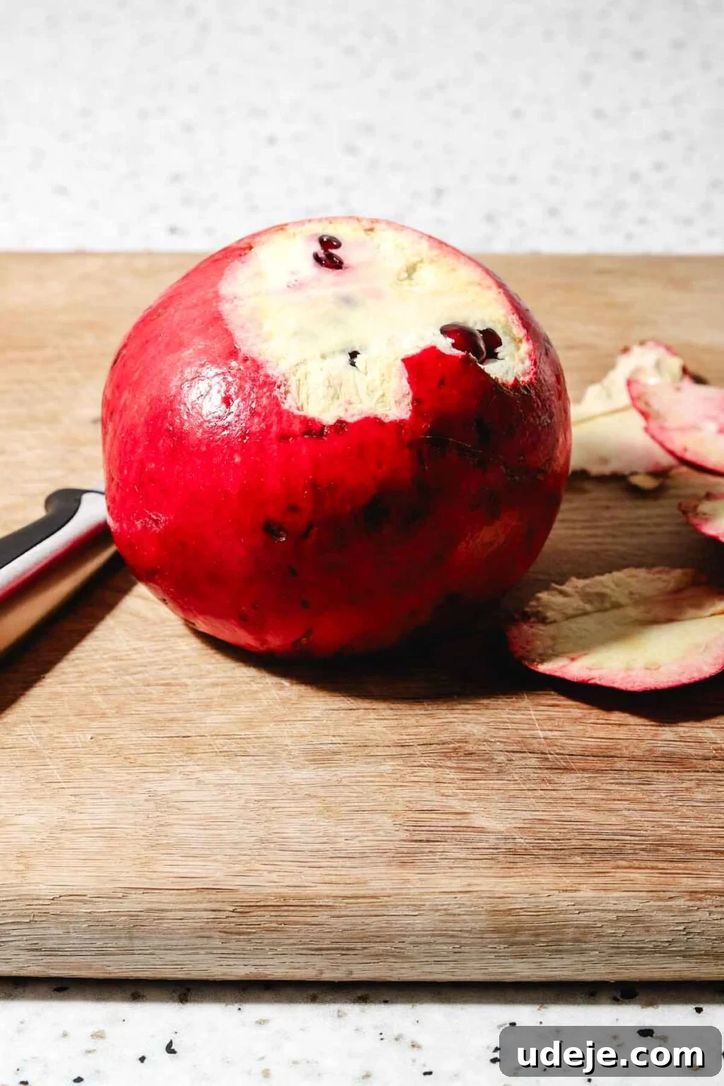 Homemade Pomegranate Molasses: Sweet, Tangy, and Versatile 8 Partly peeled pomegranate on a wooden cutting board with a knife beside it on a speckled background