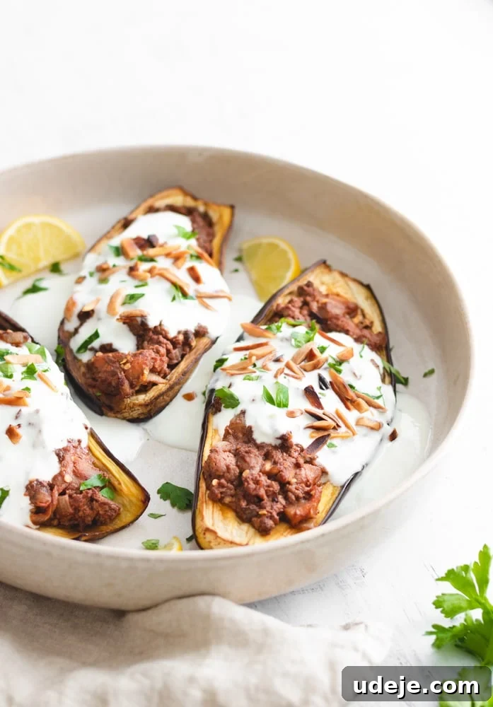 Savory Stuffed Eggplant Bake 3 Stuffed eggplants served on a plate drizzled with yogurt and garnished with toasted almonds