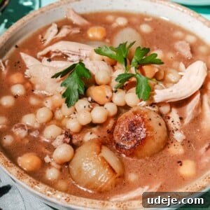 Moghrabieh stew with parsley in a light beige bowl with a green napkin and spoons on a light blue background