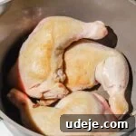Chicken leg quarters browned in a large grey and green stock pot on a marbled background