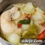 Chicken leg quarters, onion pieces, whole garlic cloves and whole carrots in water with cinnamon sticks, pepper corns and bay leaves simmering in a large grey and green stock pot