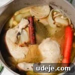 Chicken leg quarters, onion pieces, whole garlic cloves and whole carrots in water with cinnamon sticks, pepper corns and bay leaves simmering in a large grey and green stock pot