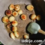 caramelized pearl onions in a large pot with a spatula inside, over an induction element