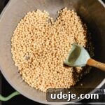moghrabieh pearl couscous uncooked in a large pot with a spatula inside, over an induction plate