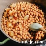 moghrabieh stew with chickpeas, pearl onions and pearl couscous inside a large pot with a spatula