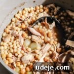 Moghrabieh stew with chicken in a large grey and green stock pot with a black ladle on a marble background