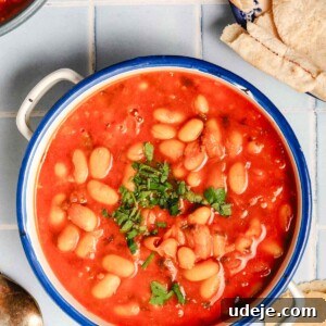 Moroccan Loubia A Flavorful Vegetarian White Bean Stew 11 Moroccan Loubia in a white handled bowl with a blue rim, pita bread on a white and blue plate with two spoons beside the loubia bowl on a light blue square tiled background