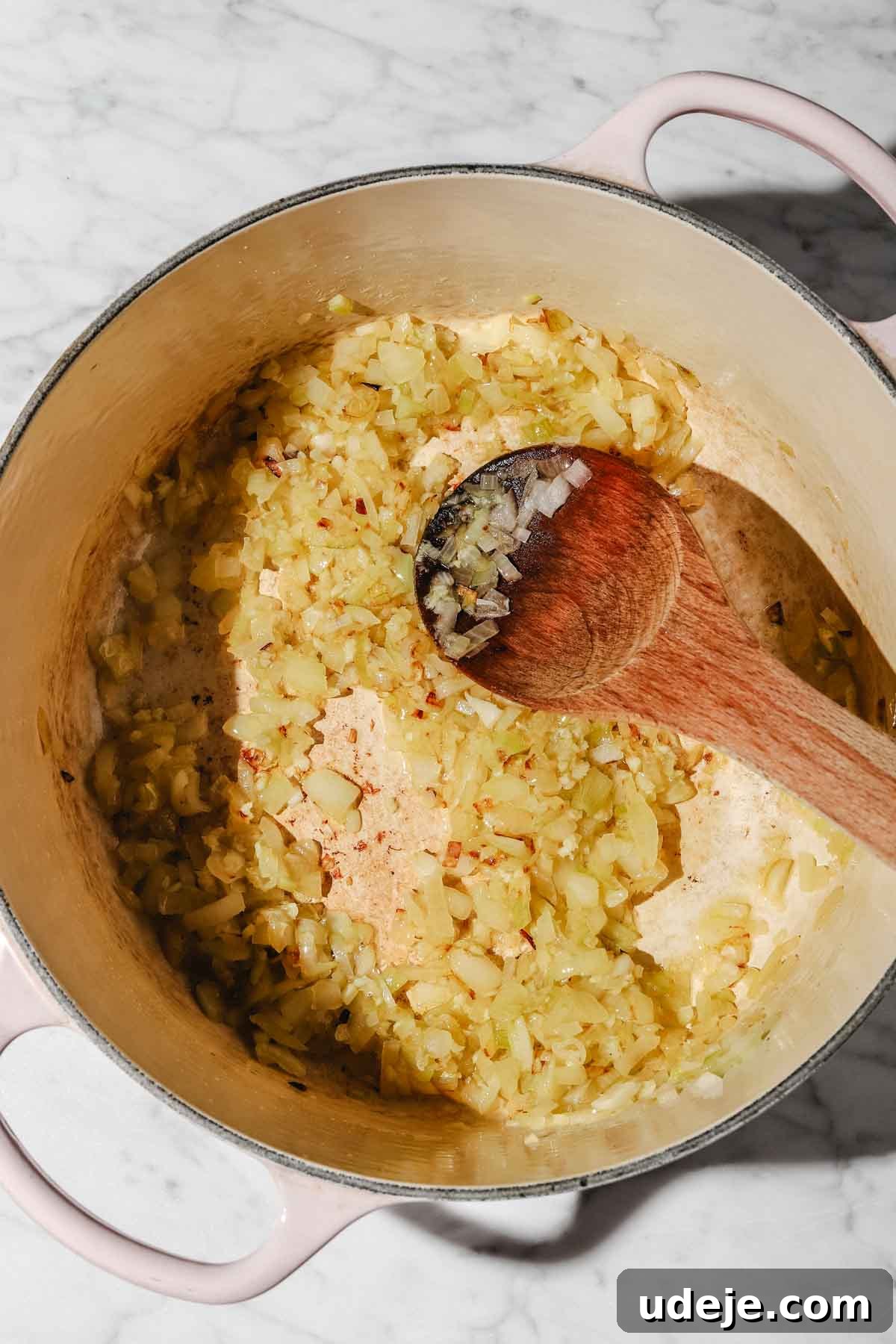 Moroccan Loubia A Flavorful Vegetarian White Bean Stew 4 Sautéed chopped onions in a large beige pot with a wooden spoon on a marble background