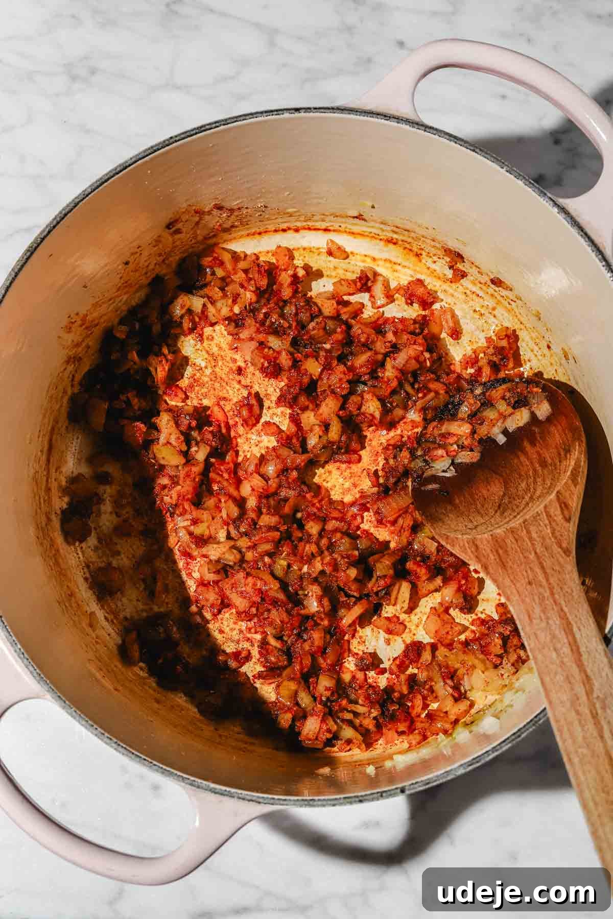 Moroccan Loubia A Flavorful Vegetarian White Bean Stew 5 Sautéed chopped onions and spices in a large beige pot with a wooden spoon on a marble