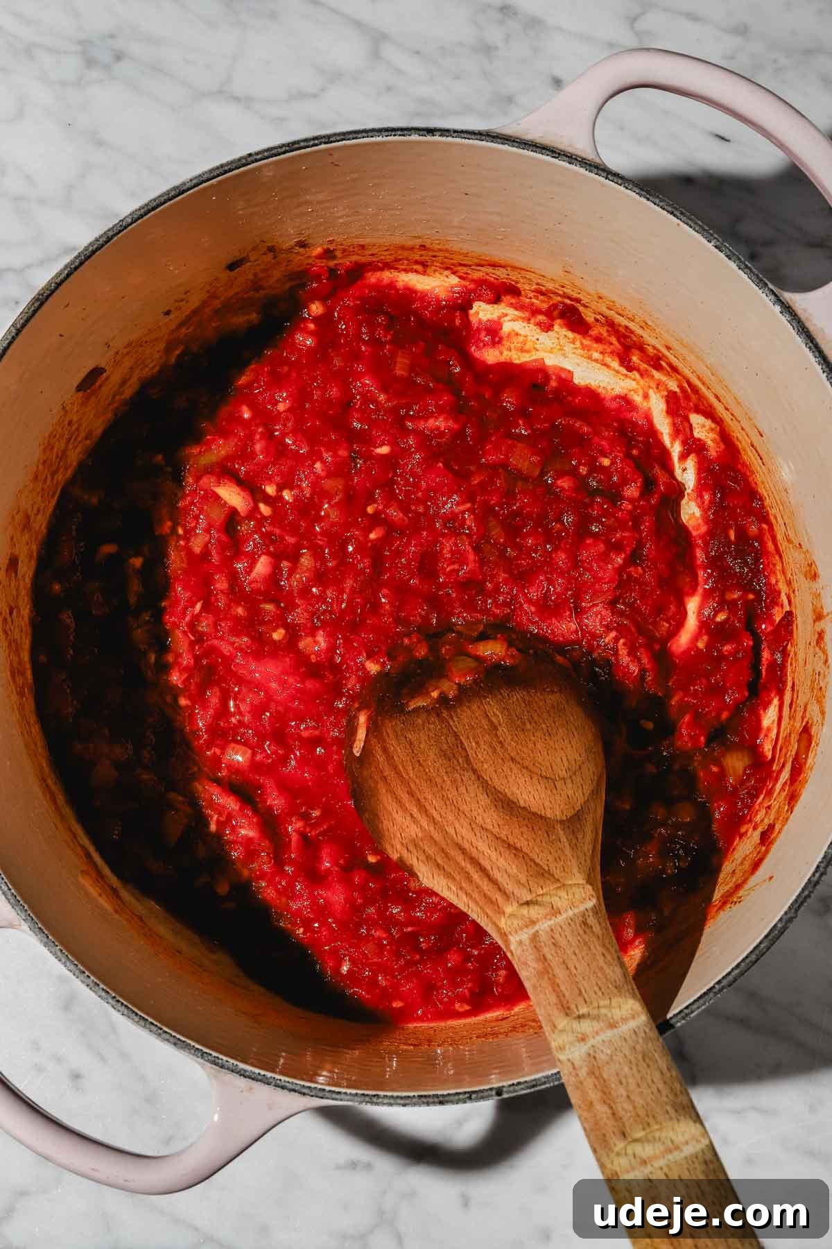 Moroccan Loubia A Flavorful Vegetarian White Bean Stew 6 Sautéed chopped onions, tomatoes and spices in a large beige pot with a wooden spoon on a marble