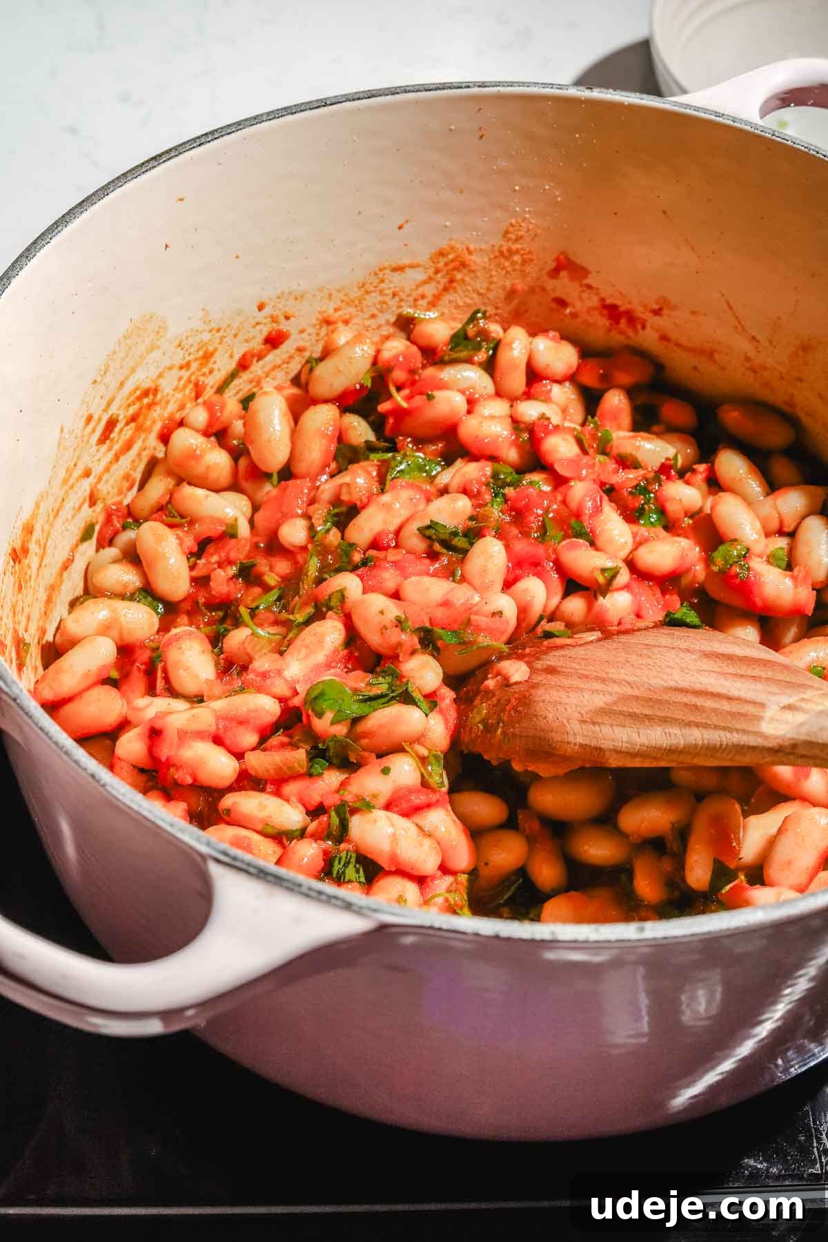 Moroccan Loubia A Flavorful Vegetarian White Bean Stew 8 Moroccan loubia in a large beige pot with a wooden spoon on a marble background