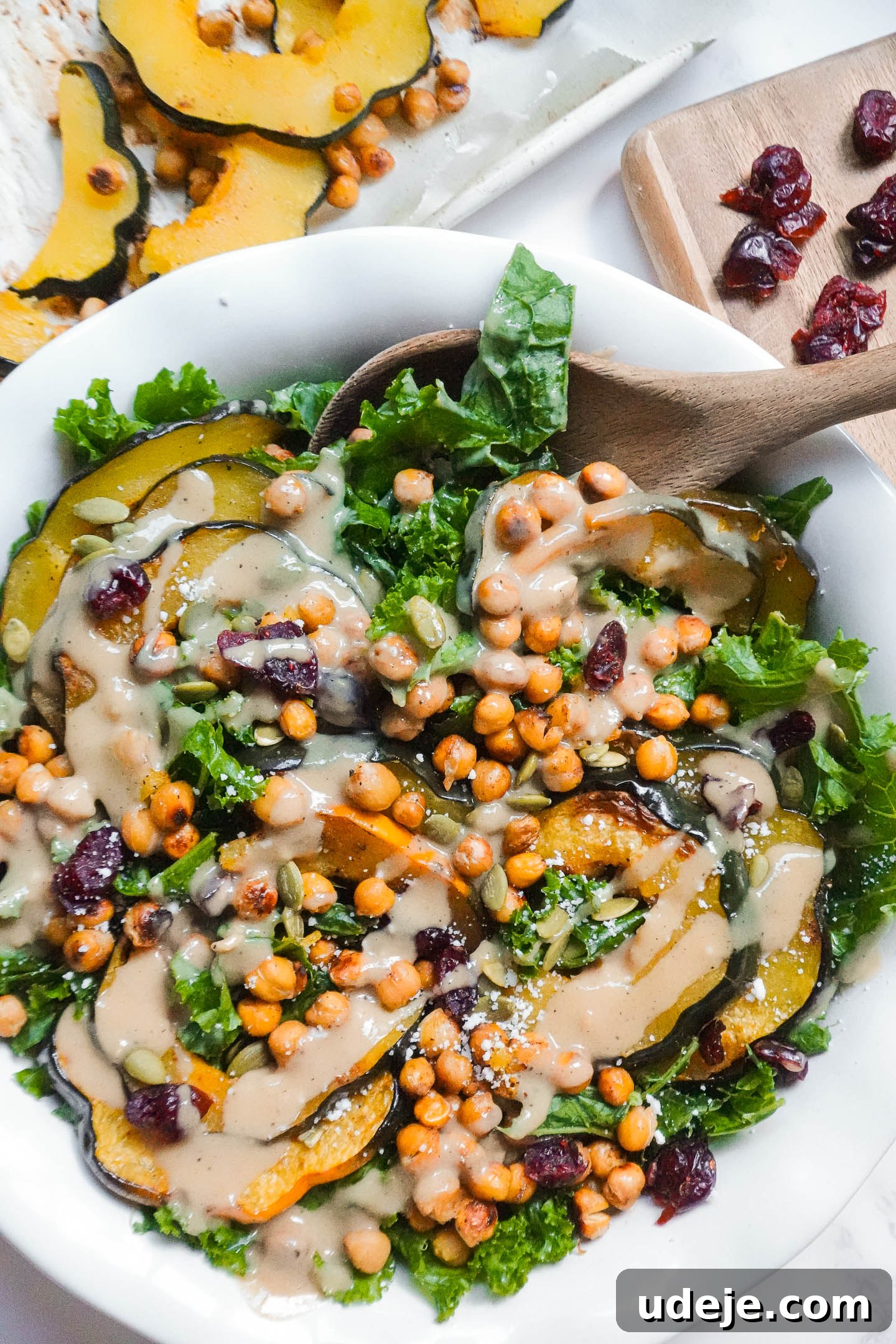 Roasted Acorn & Kale Salad with Maple Tahini 2 A vibrant fall kale salad with roasted acorn squash, crispy chickpeas, dried cranberries, and pumpkin seeds, dressed in a creamy maple tahini dressing, served in a white bowl.