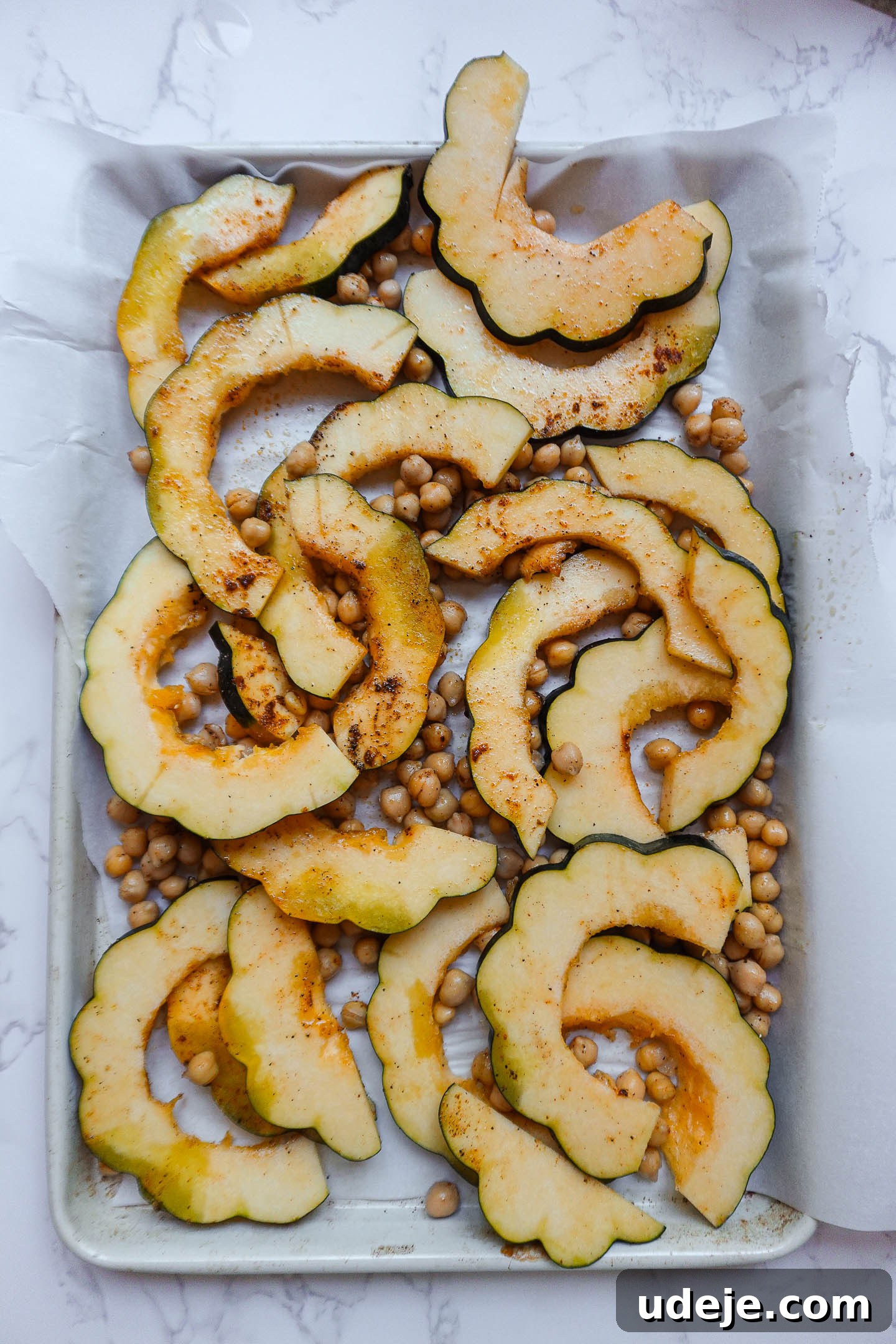 Roasted Acorn & Kale Salad with Maple Tahini 3 Sliced acorn squash and chickpeas coated in spices on a baking sheet, ready for roasting.