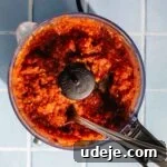 Blended tomato, onion and garlic spice paste in a food processor with a metal spoon on a blue tiled background
