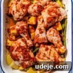 Chicken, cubed potatoes and trimmed green beans mixed with blended spice mixture in a white and blue rimmed baking pan on a blue tiled background