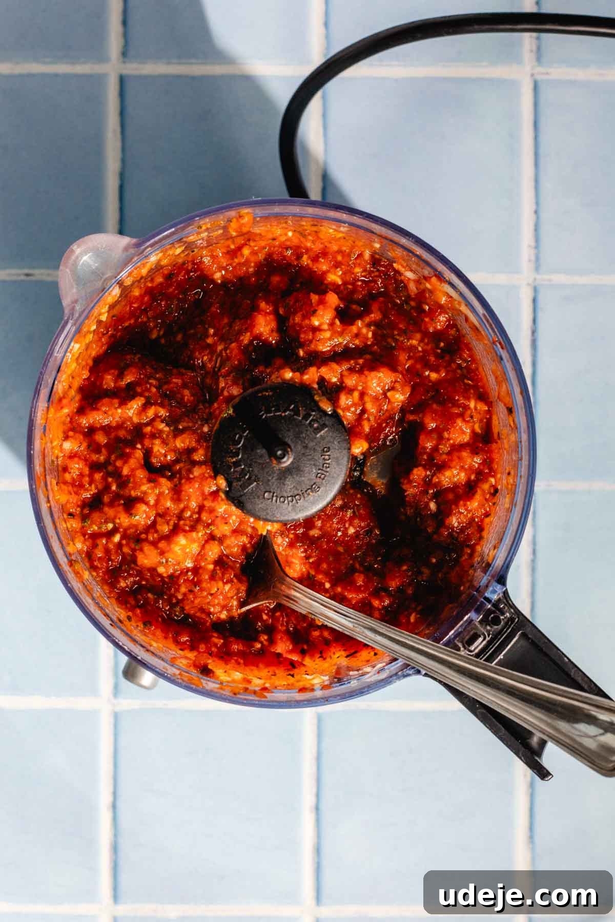 Irresistible Mediterranean Oven-Roasted Chicken 6 Blended tomato, onion and garlic spice paste in a food processor with a metal spoon on a blue tiled background