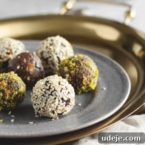 Wholesome Cardamom and Tahini Date Bliss Balls 4 A close-up of assorted energy date balls coated in sesame seeds and ground pistachios, arranged on a gray plate atop a gold tray with a beige cloth underneath—an inviting display inspired by a classic date balls recipe.