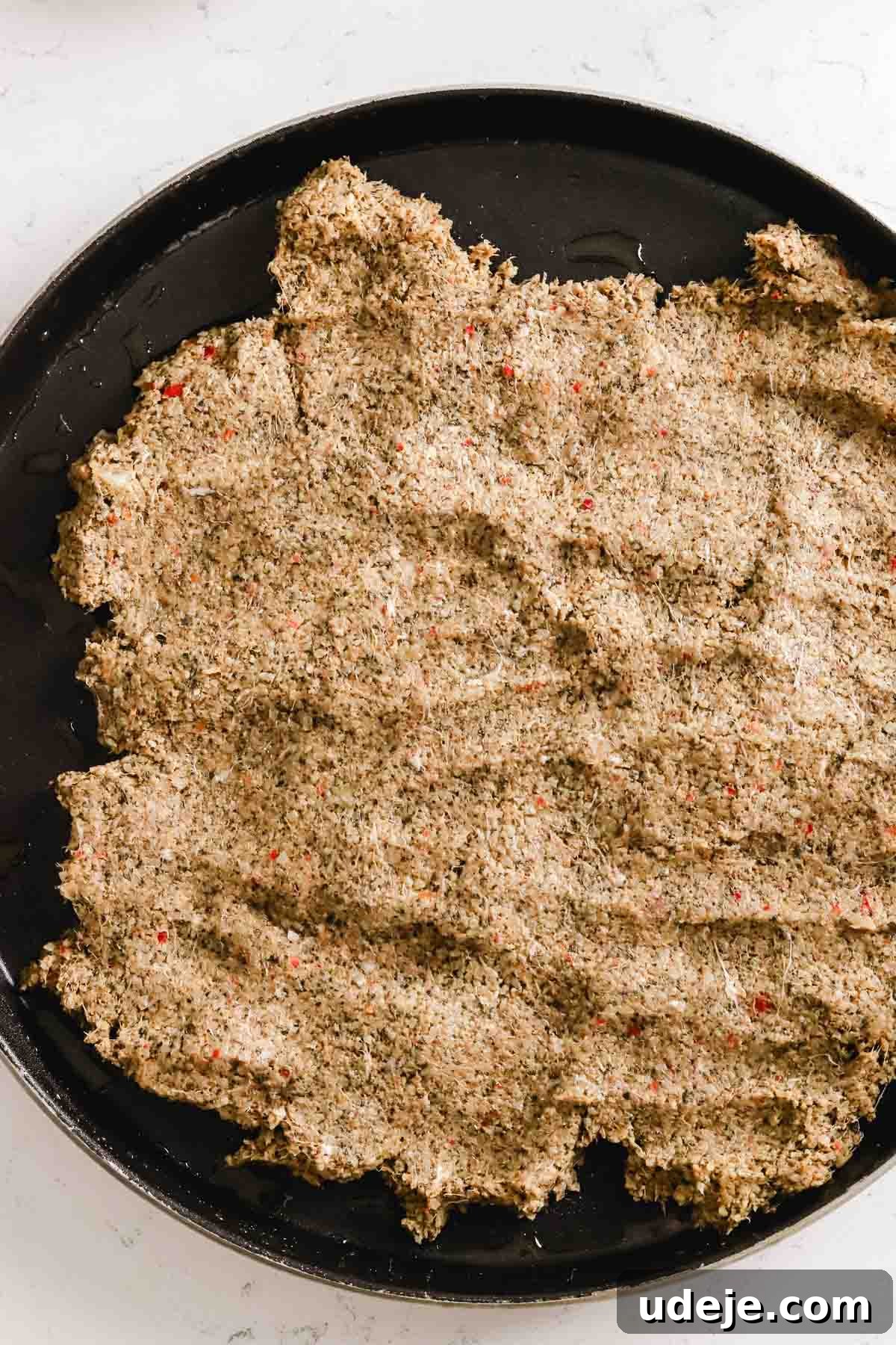 Baked Kibbeh Casserole 14 Kibbeh dough being carefully spread out and pressed into a large circular baking tray on a light marble background, forming the base layer.