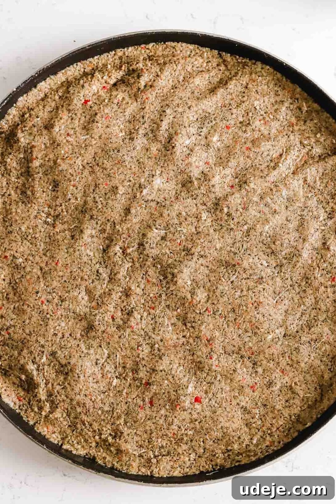 Baked Kibbeh Casserole 15 Fully spread out and smoothed kibbeh dough creating a uniform base layer in a circular baking pan on a light marble background.
