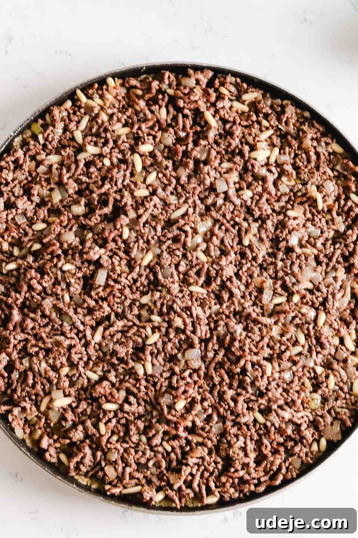 Baked Kibbeh Casserole 17 Sautéed ground beef and onions spread out evenly over the kibbeh dough on a round circular baking pan, creating a smooth layer of filling.