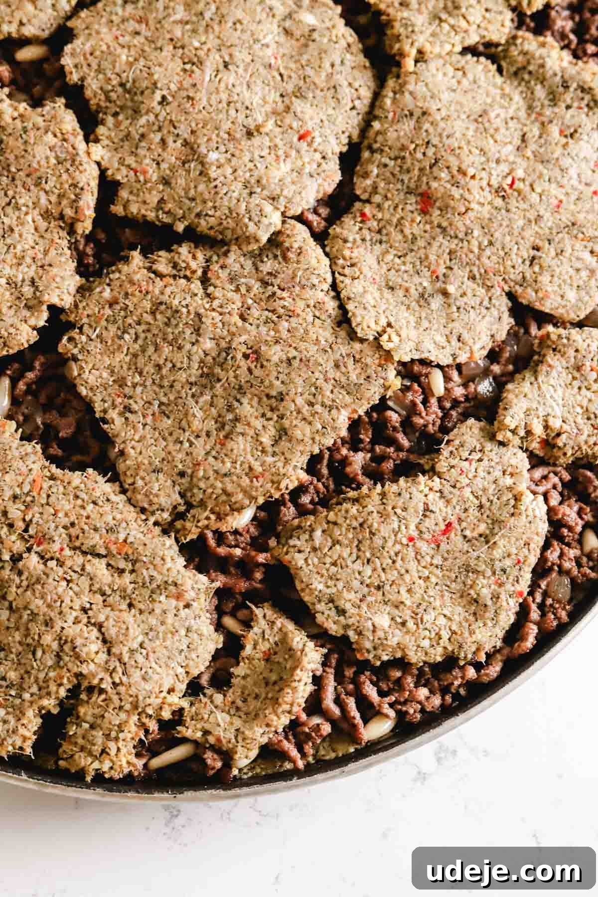 Baked Kibbeh Casserole 18 Small, circular pieces of kibbeh dough meticulously placed on top of the sautéed ground beef and onions in a circular baking pan, preparing for the top layer.
