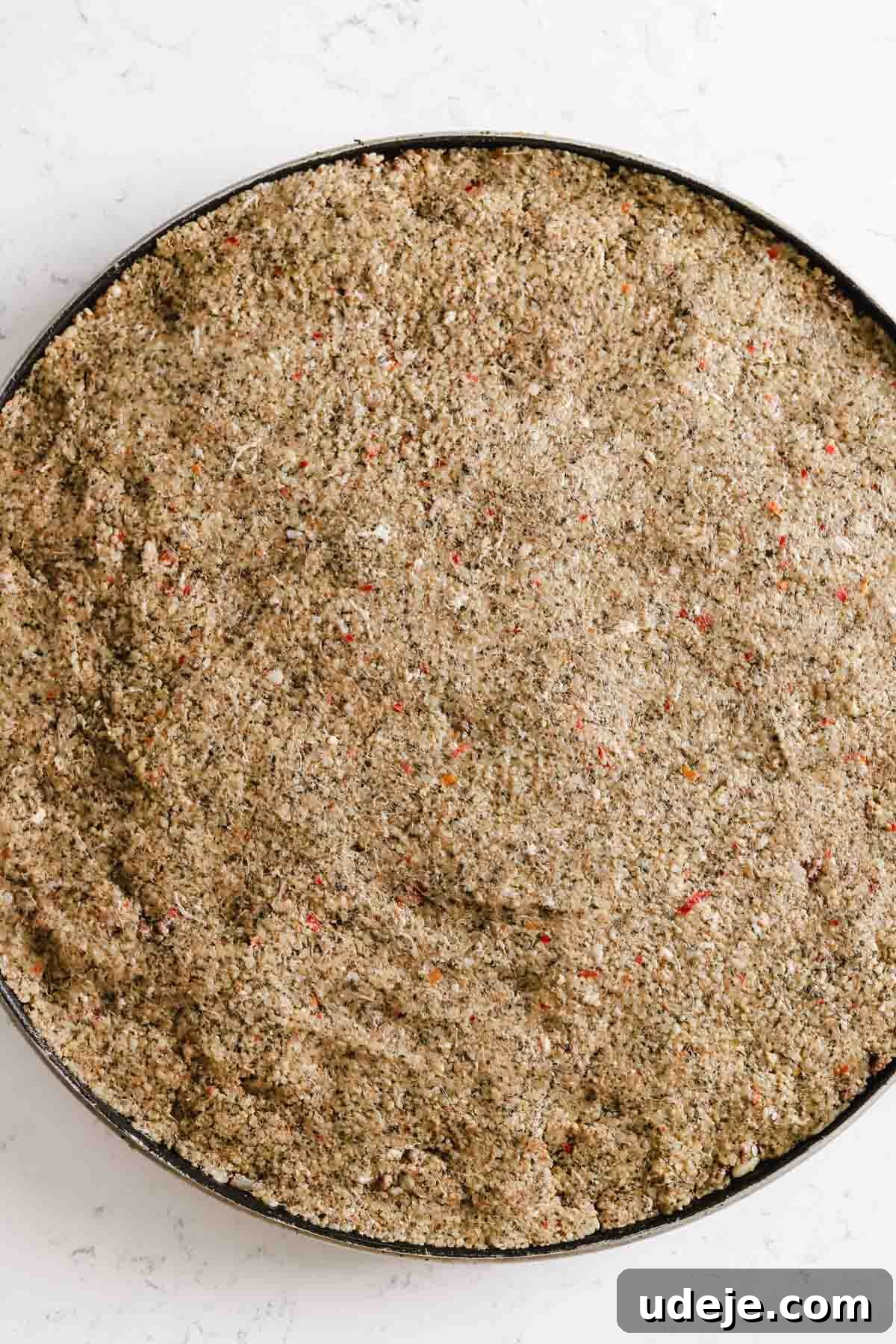 Baked Kibbeh Casserole 19 Unbaked Kibbeh bil Sanieh with a smooth, even top layer of dough in a large circular baking pan on a light marble surface, ready for scoring.