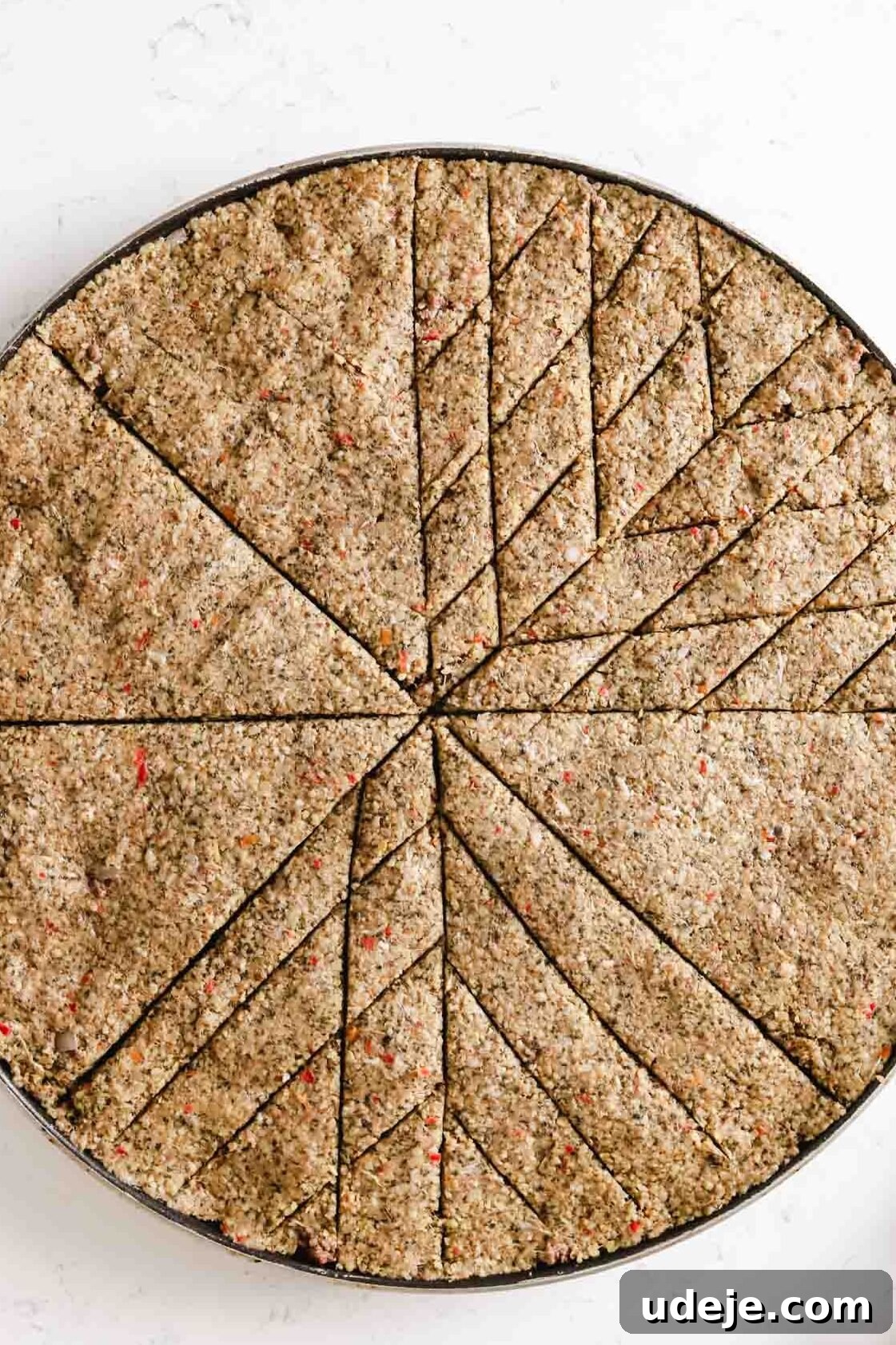Baked Kibbeh Casserole 22 Unbaked Kibbeh bil Sanieh showcasing fully scored intricate diamond shapes on half of its surface in a large circular baking pan on a light marble surface, detailing the pattern.