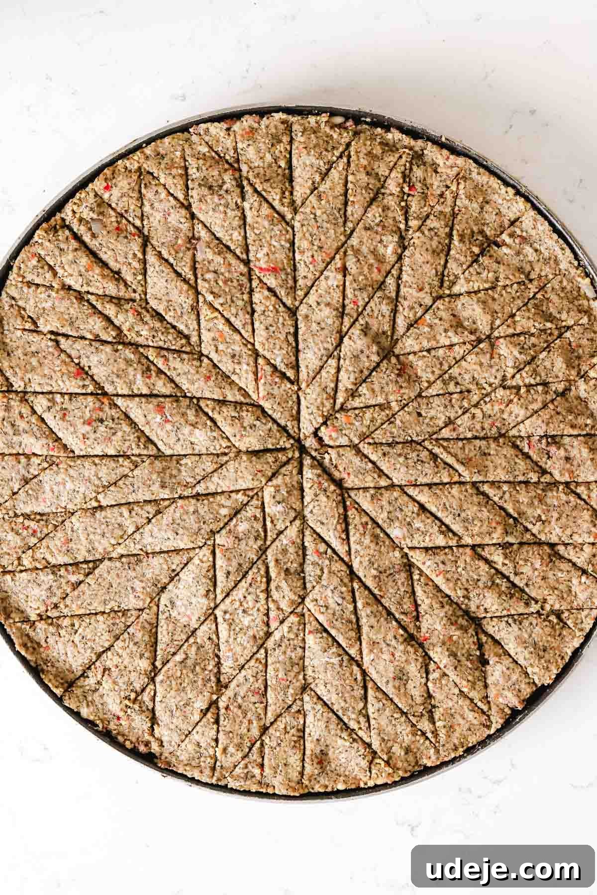 Baked Kibbeh Casserole 23 Unbaked Kibbeh bil Sanieh elegantly cut into diamond shapes in a large circular baking pan on a light marble surface, demonstrating a simpler decorative pattern.