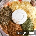 Food processor with onions and red peppers finely chopped with find bulgur, dried basil and dried mint leaves and kamouneh spice on top on a white background