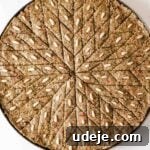 Unbaked Kibbeh bil sanieh cut into diamond shapes with pine nuts on each piece in a large circular baking pan on a light marble surface