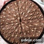 Baked Kibbeh bil Sanieh in a large circular baking tray on a pink terrazzo background with a pink towel in the corner, light blue plates with cutlery and a small bowl with yogurt and mint leaves