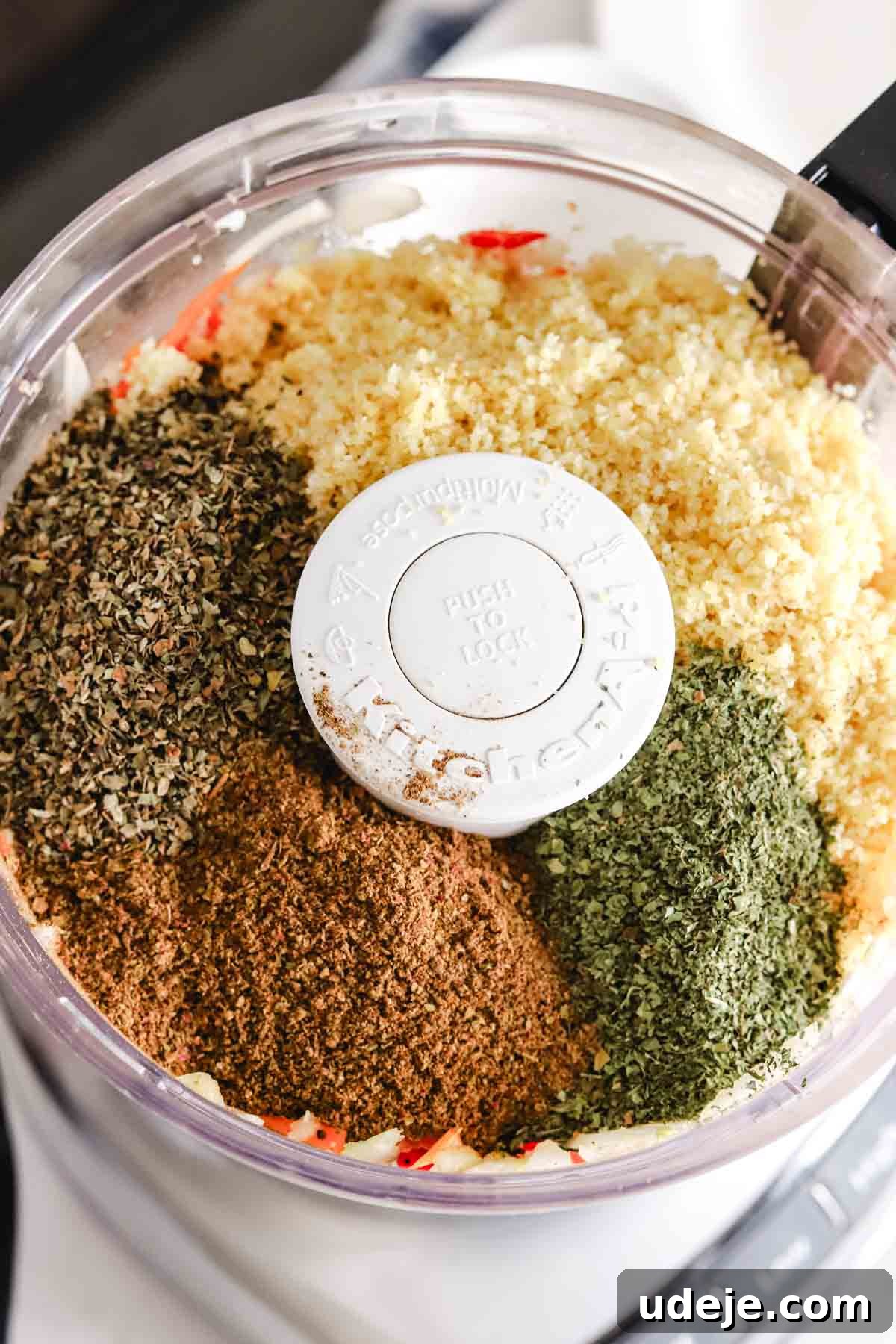 Baked Kibbeh Casserole 9 Finely chopped onions and red peppers with bulgur, dried basil, dried mint leaves, and kamouneh spice on top in a food processor, showing the addition of all dry ingredients.