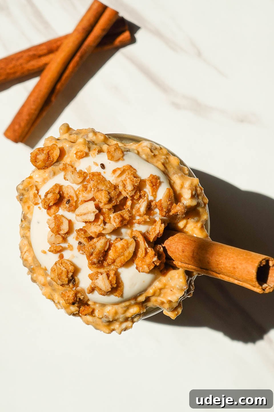 Autumn Spiced Overnight Oats 3 Overhead shot of vegan pumpkin overnight oats swirled with non-dairy yogurt, topped with crunchy granola and a dusting of cinnamon, emphasizing texture and appeal.