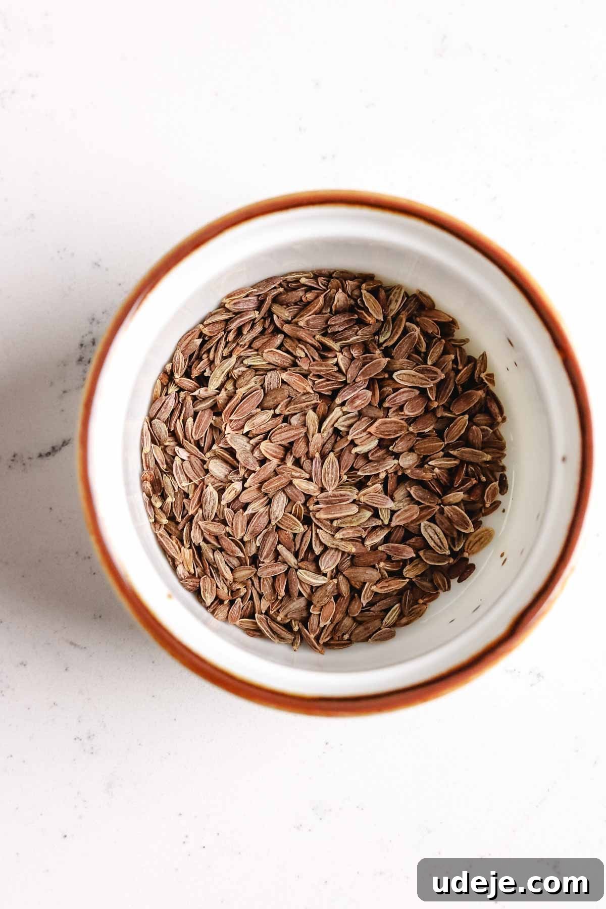 A small white bowl holds a collection of aromatic dill seeds, ready to be incorporated into the maftoul dish.