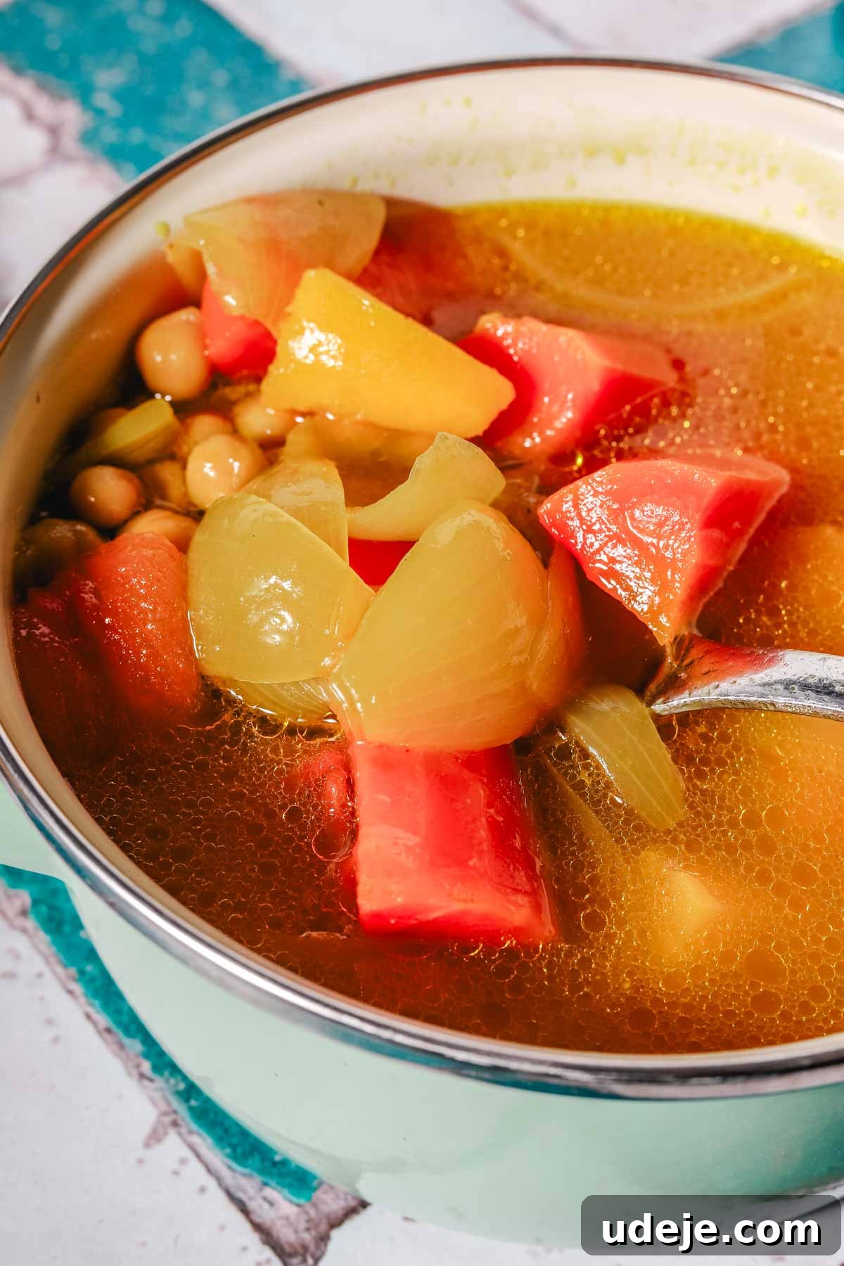 A comforting bowl of chicken stock soup, richly laden with large, chunky vegetables including vibrant carrots, tender squash, sweet onions, and hearty chickpeas, promises a nourishing meal.